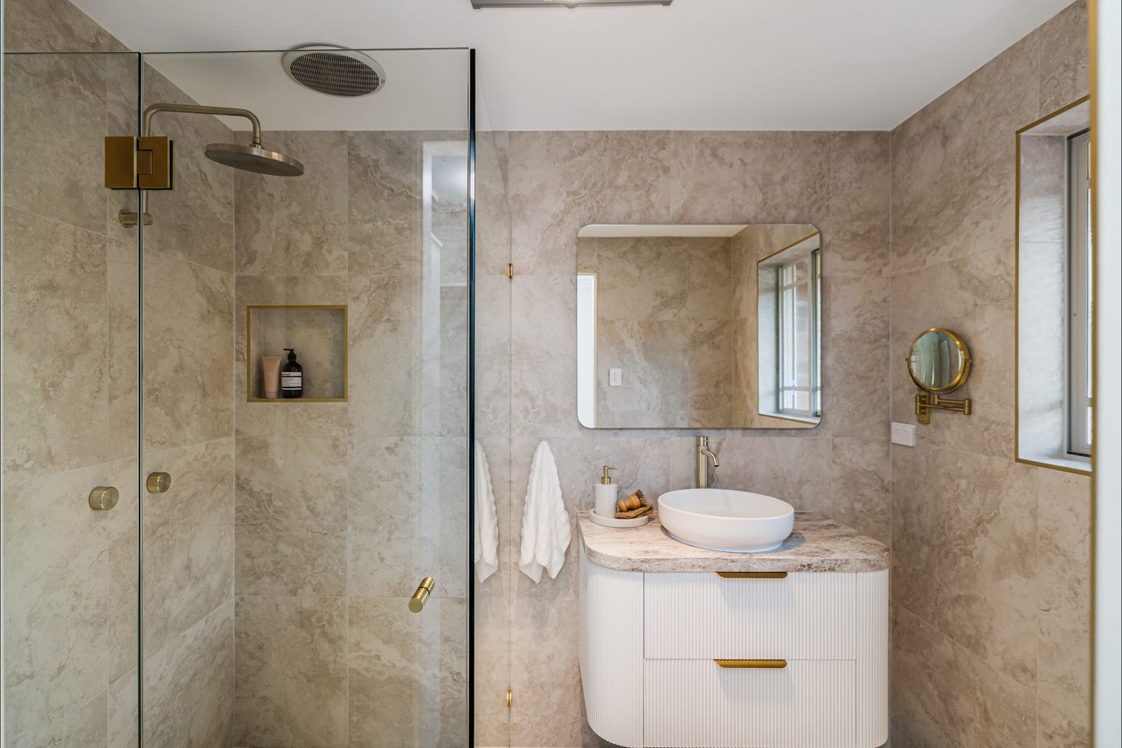 Padstow Heights bathroom with warm stone-look tiles, brushed brass fittings and a curved fluted vanity