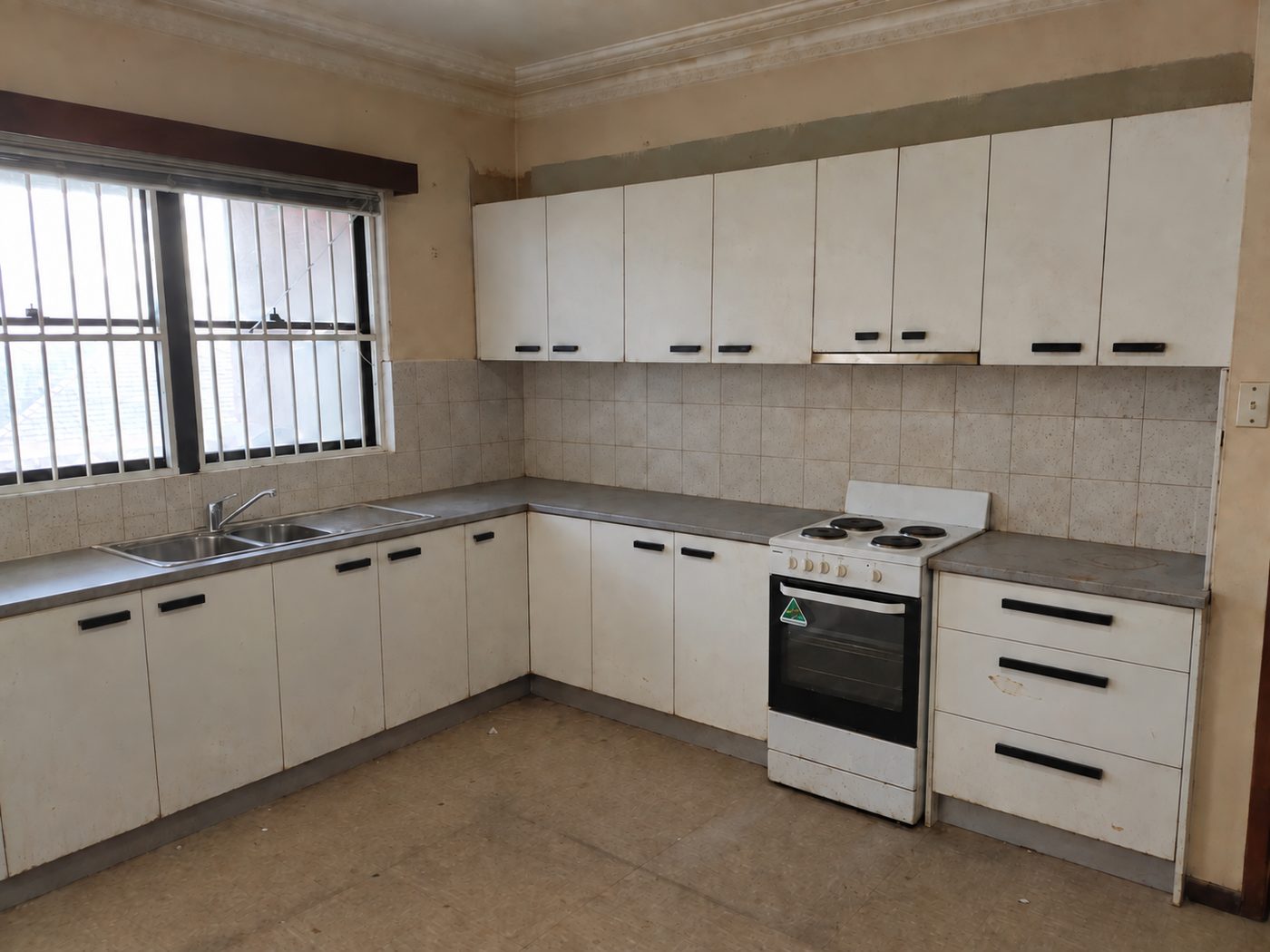 Padstow kitchen before renovation, with dated white cabinets, small wall tiles and a worn floor