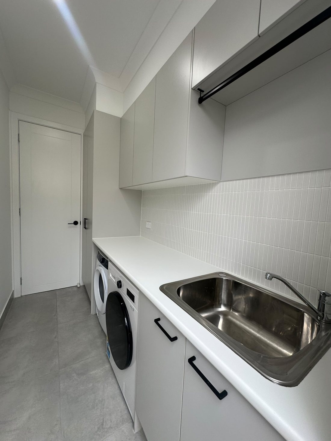 Peakhurst laundry with white cabinetry, hanging rail and stainless steel sink